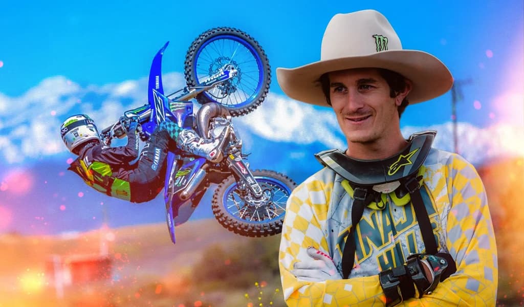 A freestyle motocross rider, Jarryd McNeil, standing with arms crossed while another rider performs an aerial trick in the background.