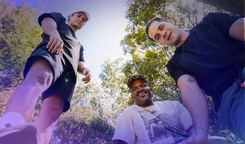 Three men standing outdoors, smiling while looking down towards the camera.