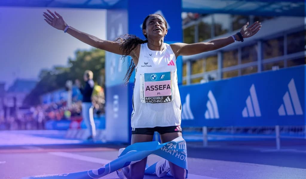 Female runner kneels at the finish line with arms raised as a race banner wraps around her legs.