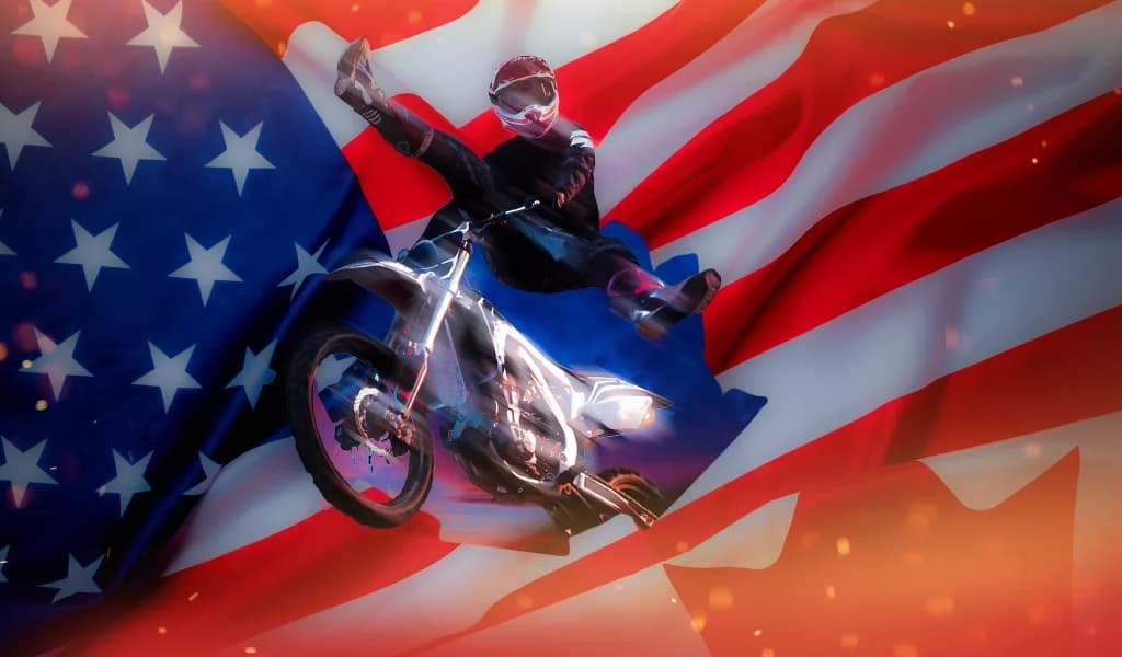 Motocross rider performing an aerial trick in front of blended American and Canadian flags.
