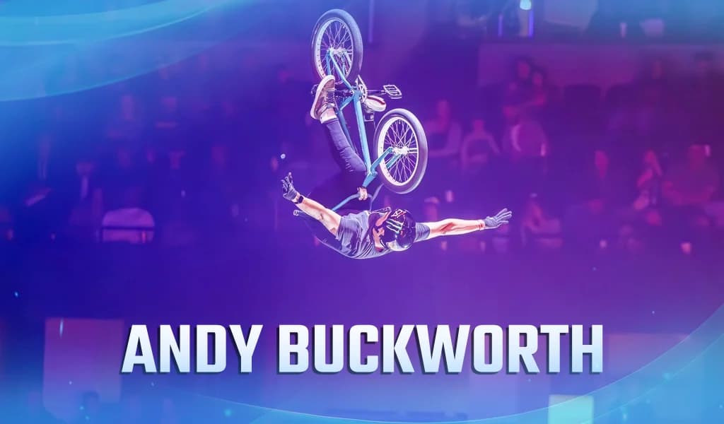 BMX rider upside down midair with arms extended as his bike rotates beneath him inside a packed arena.
