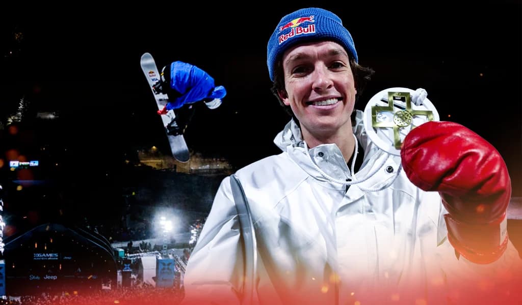 Scotty James holding an X Games medal while a snowboarder jumps in the background at a nighttime competition.