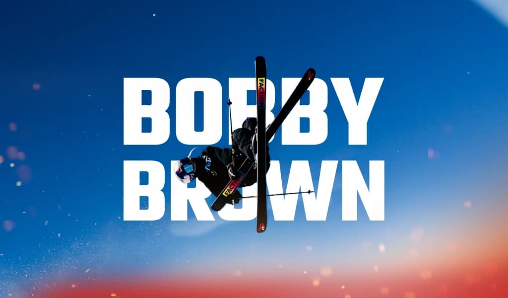 Bobby Brown performing a freestyle skiing trick midair with skis crossed, shown over a blue background with his name displayed.